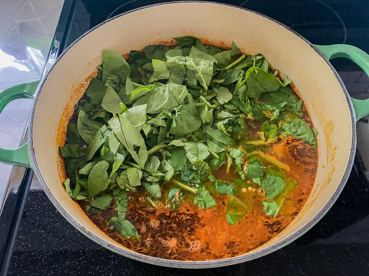 Spinach in a green soup pot on a black stovetop.