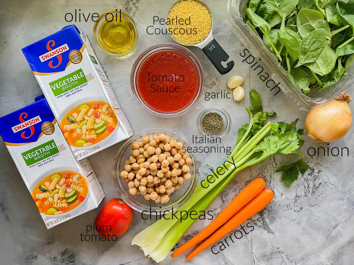 Ingredients on marble countertop: broth, oil, couscous, tomato sauce, chickpeas, tomatoes, garlic, spinach, onion, carrots, and celery.