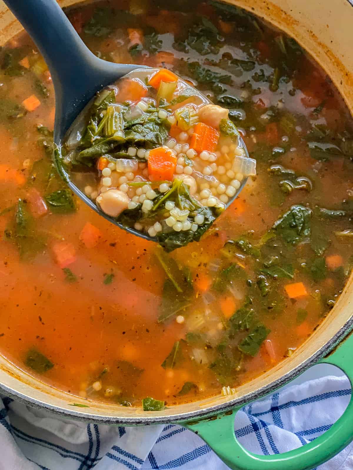 Black ladle holding vegetable soup over a green pot.