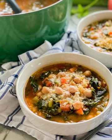 Two white bowls filled with veggies soup with chickpeas and a green pot in the background.