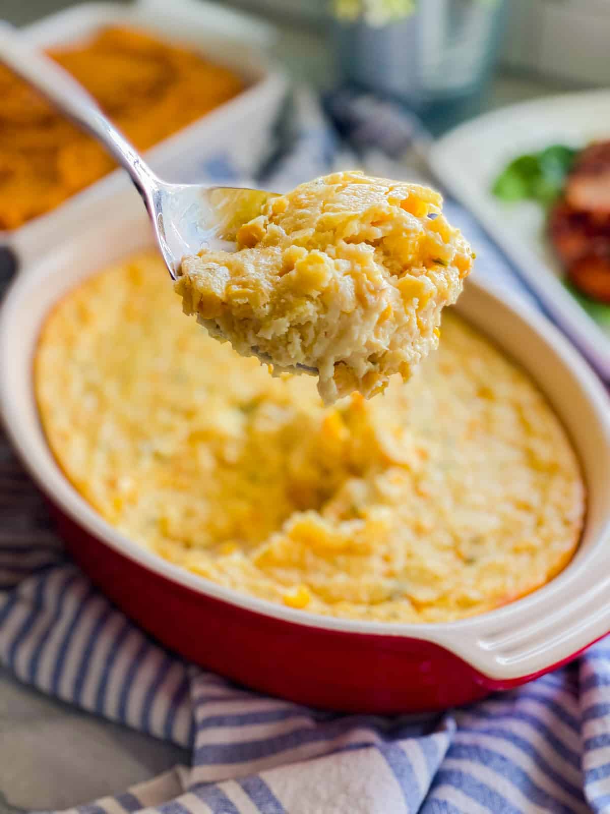 Red oval baking dish with corn cassserole on a spoon.