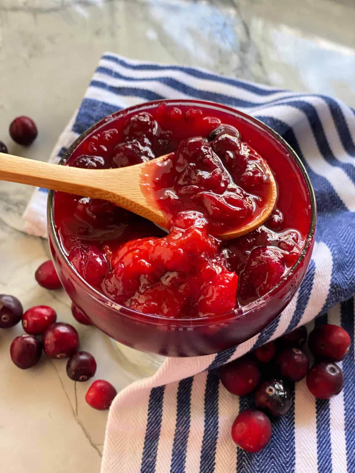 Wooden spoonin a glass bowl filled with cranberry sauce.