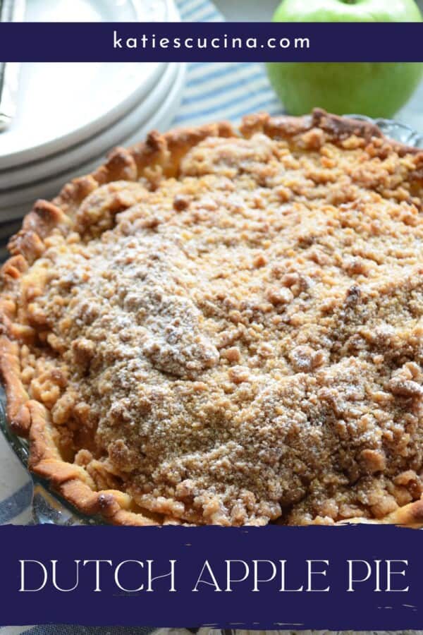 Pie with crumb topping with white plates stacked in the background and a green apple with recipe title text on image for Pinterest.