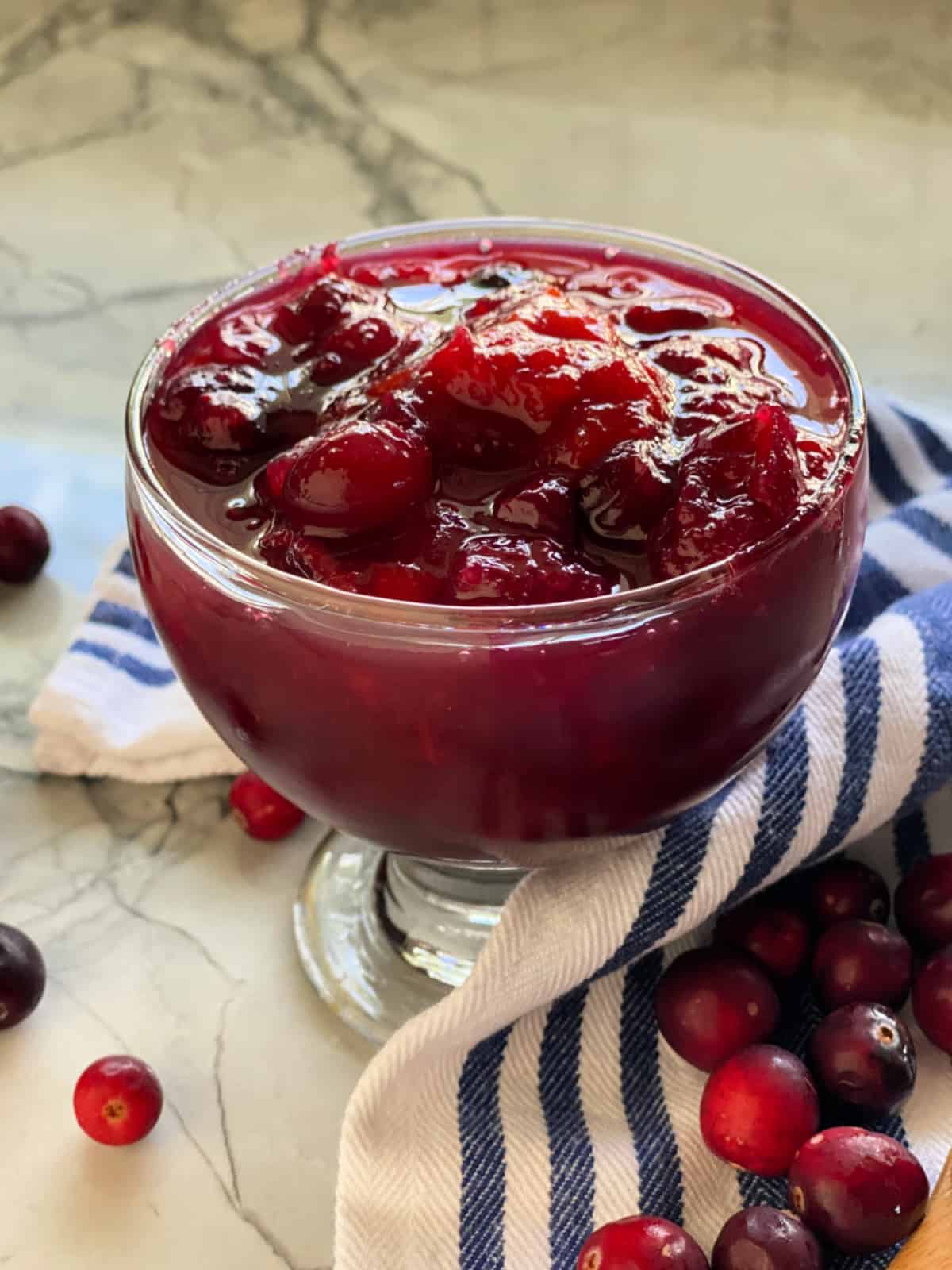 Glass dish filled with cranberry sauce with a white and blue striped cloth around it.