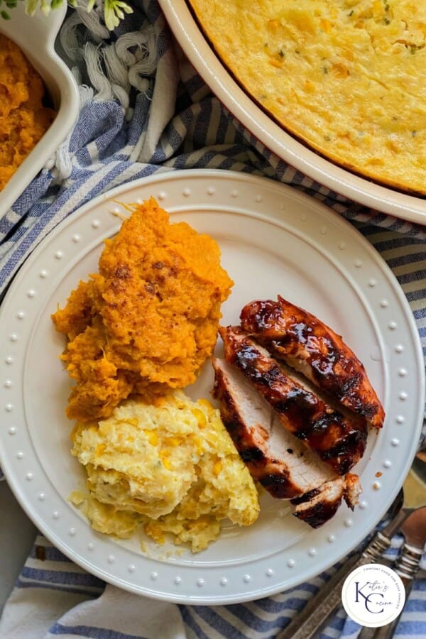 White plate filled with sliced turkey, sweet potatoes, and corn casserole with logo on right corner.