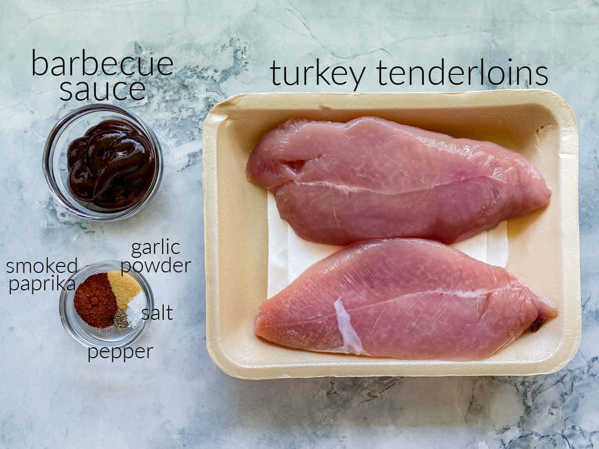 Ingredients on marble countertop: turkey tenderloin; barbecue sauce, smoked paprika, garlic powder, salt, and pepper.