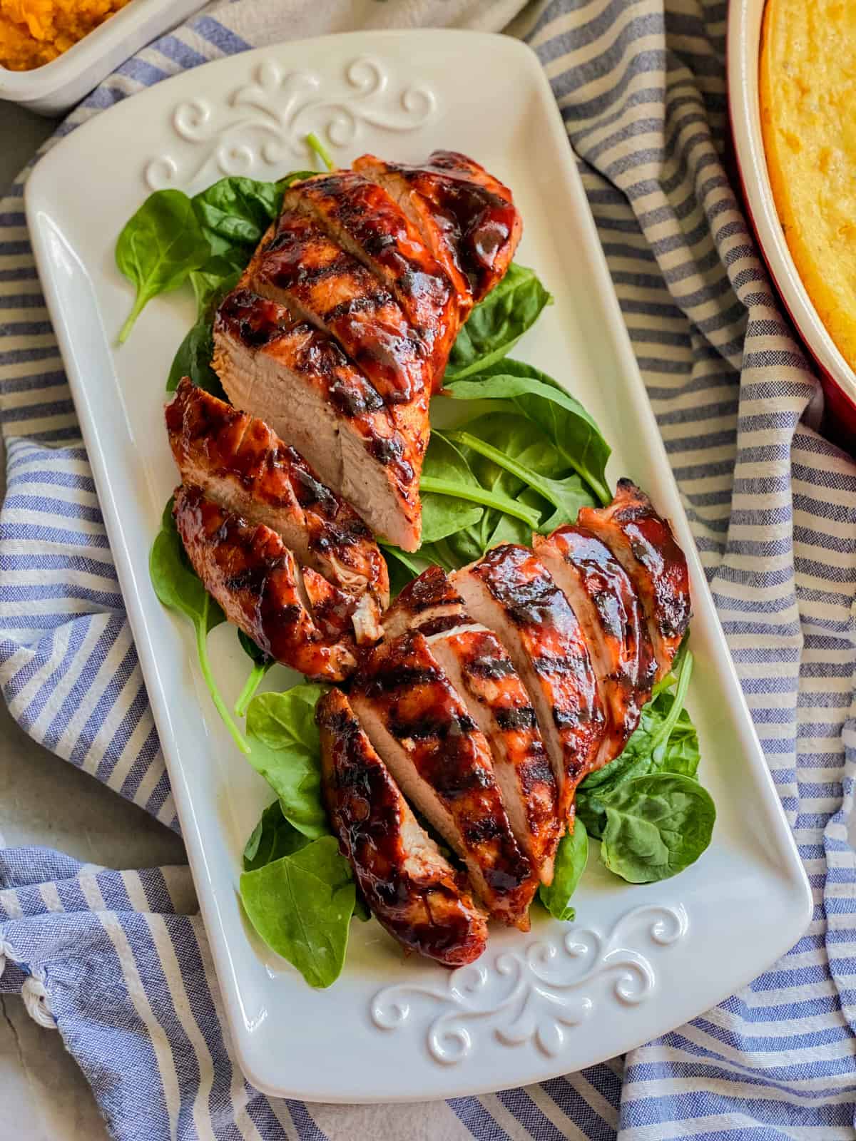 White platter with sliced meat on top of spinach leaves.