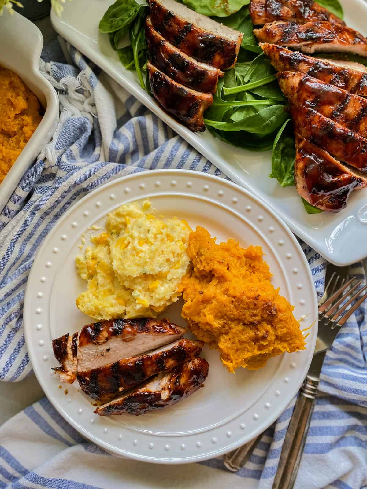 White plate filled with sweet potatoes, corn casserole, and turkey with a platter of turkey next to it.