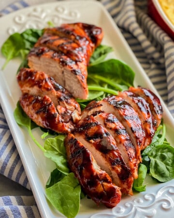 White platter sitting on top of a white and blue stripped cloth with turkey sliced on top of spinach.