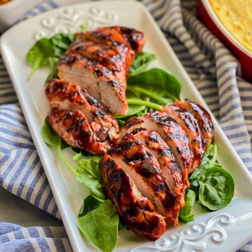 White platter sitting on top of a white and blue stripped cloth with turkey sliced on top of spinach.