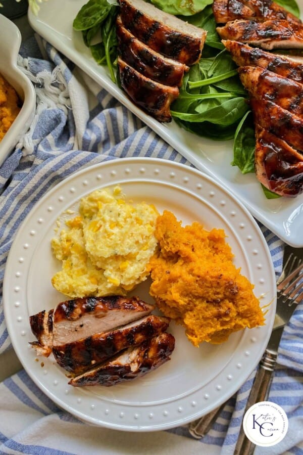 White plate with sliced turkey, corn casserole, and sweet potatoes on a blue and white striped cloth.