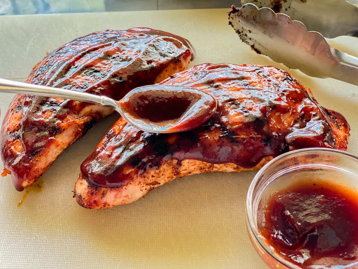 Spoon with barbecue sauce on top of turkey tenderloins on a cutting board.