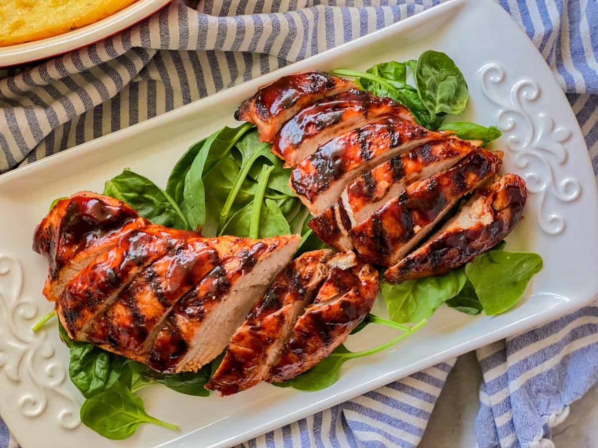 White platter with spianch leaves and sliced barbecue sauce turkey on top.