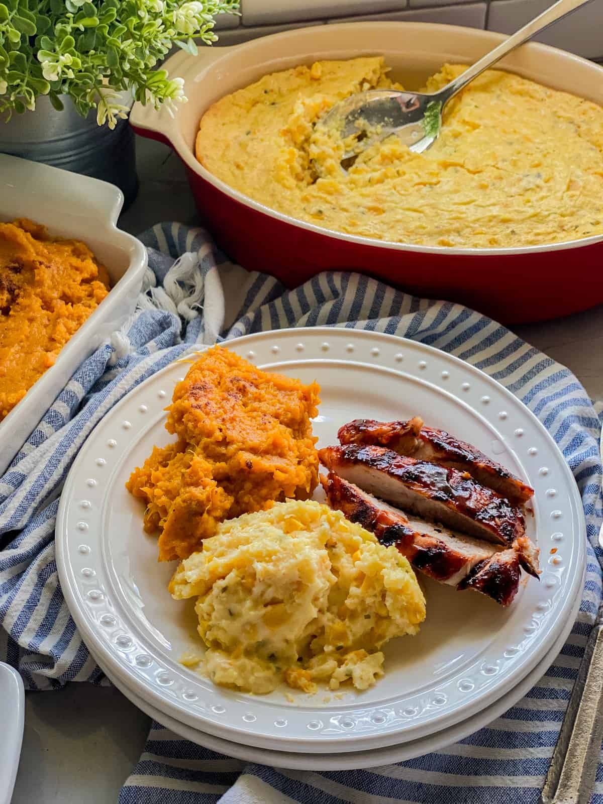 Two white plate stacked with corn casserole, sweet potatoes, and sliced turkey with corn casserole in background.