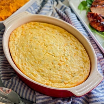 Oval red baking dish filled with corn casserole.
