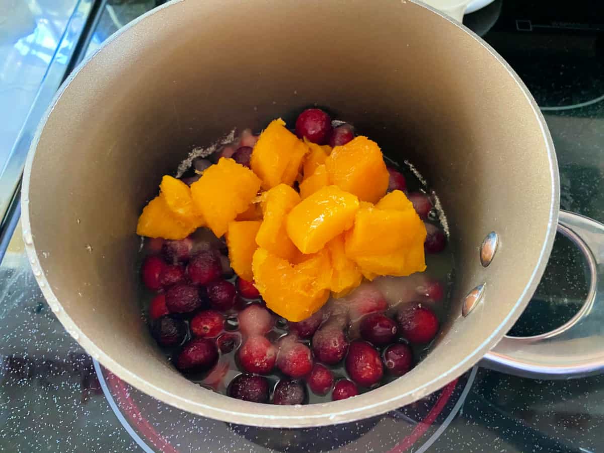 Brown pot filled with fresh cranberries, mangos, and liquid on a stove top.