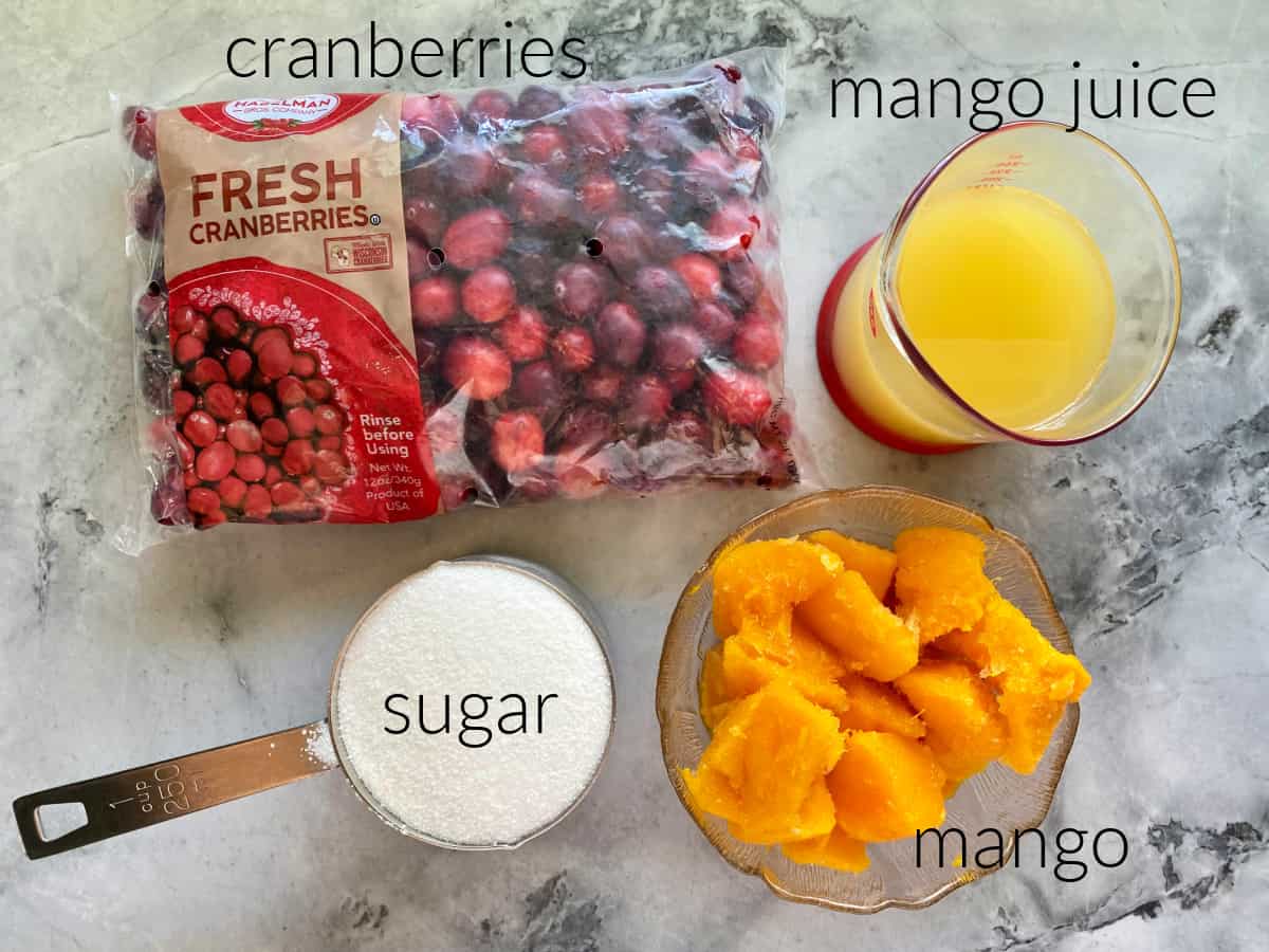 Ingrediets on counter; fresh cranberries, mango juice, sugar, and mango.