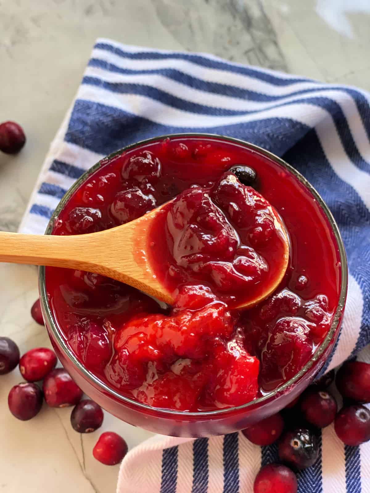 Wooden spoon dipped in a glass bowl filled with cranberry sauce.