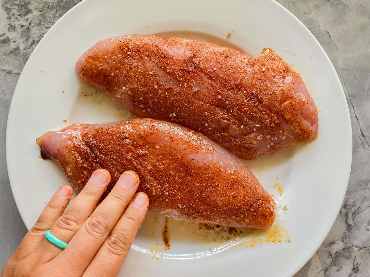 Hand massaging seasoning on to turkey tenderloin on a white plate.