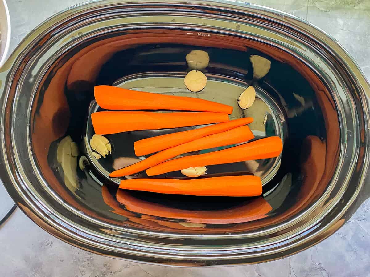 Black oval slow cooker with carrots and garlic cloves.