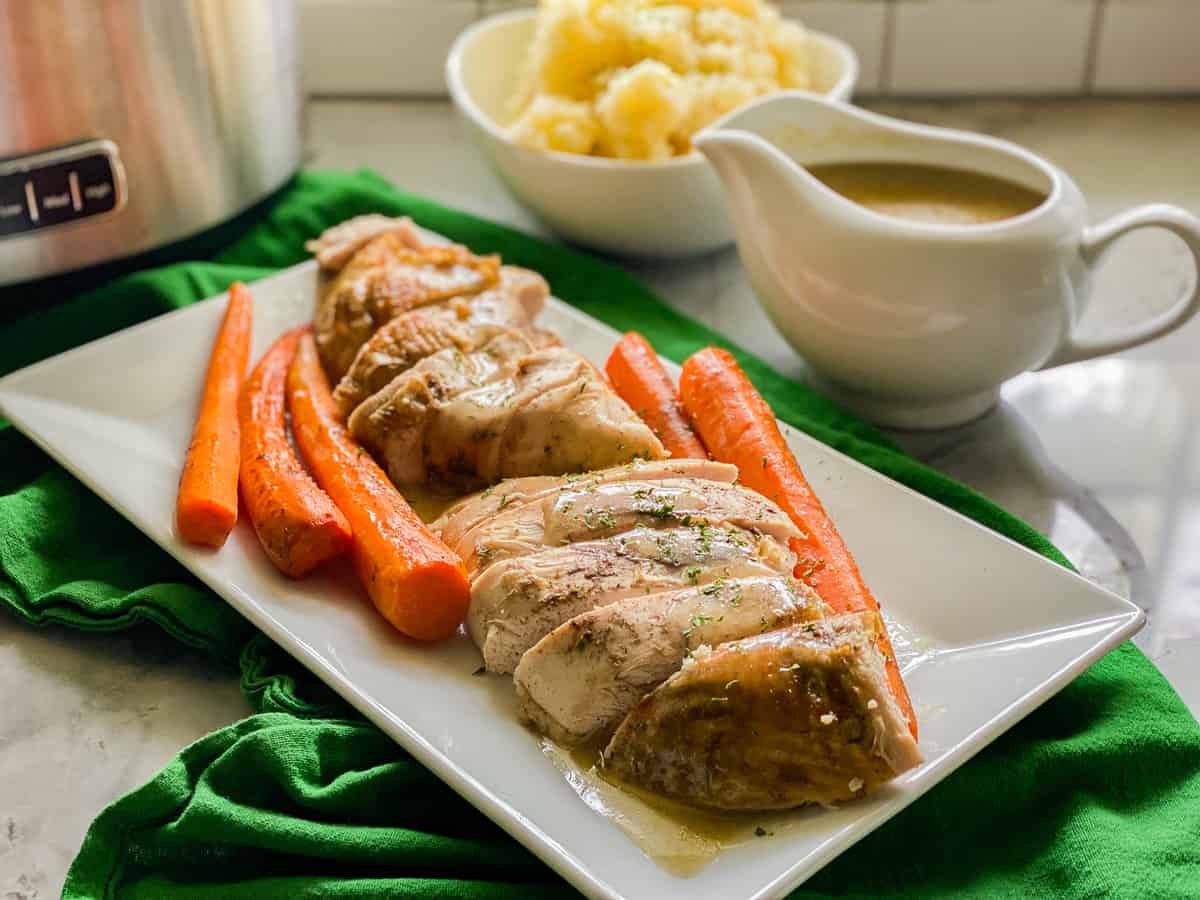 White rectangular dish filled with slices of turkey breast and carrots with mashed potatoes and gravy in the background.