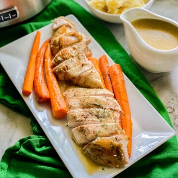 White platter filled with sliced turkey and carrots with gravy poured on top.