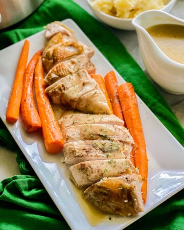 White platter filled with sliced turkey and carrots with gravy poured on top.