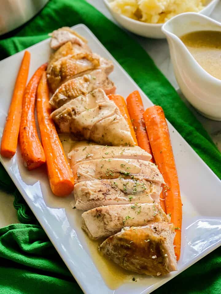 White platter filled with sliced turkey and carrots with gravy poured on top.