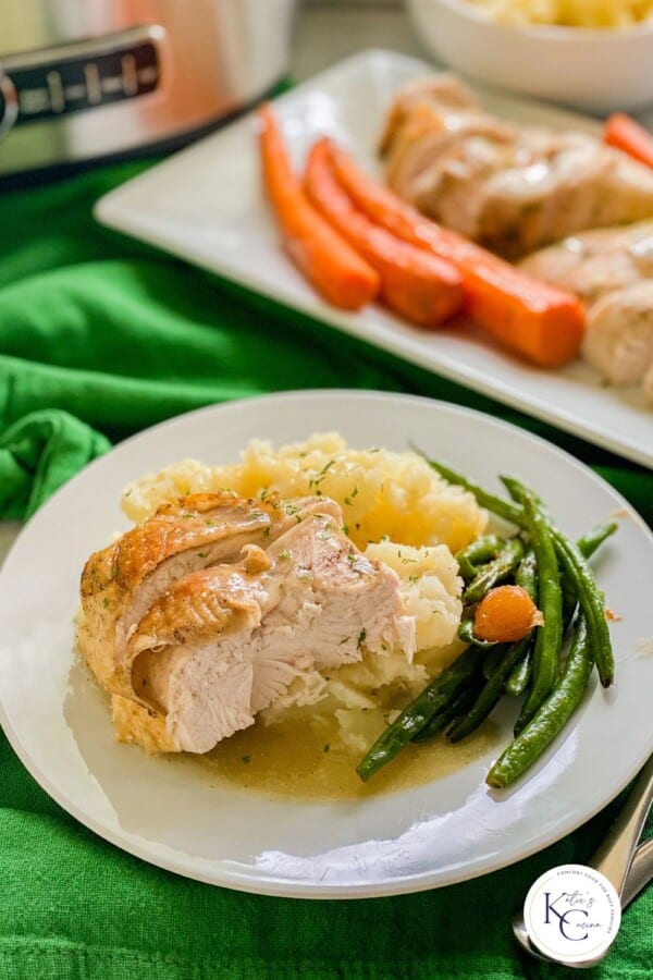 White plate filled with sliced turkey, mashed potatoes, and green beans with logo on right corner.