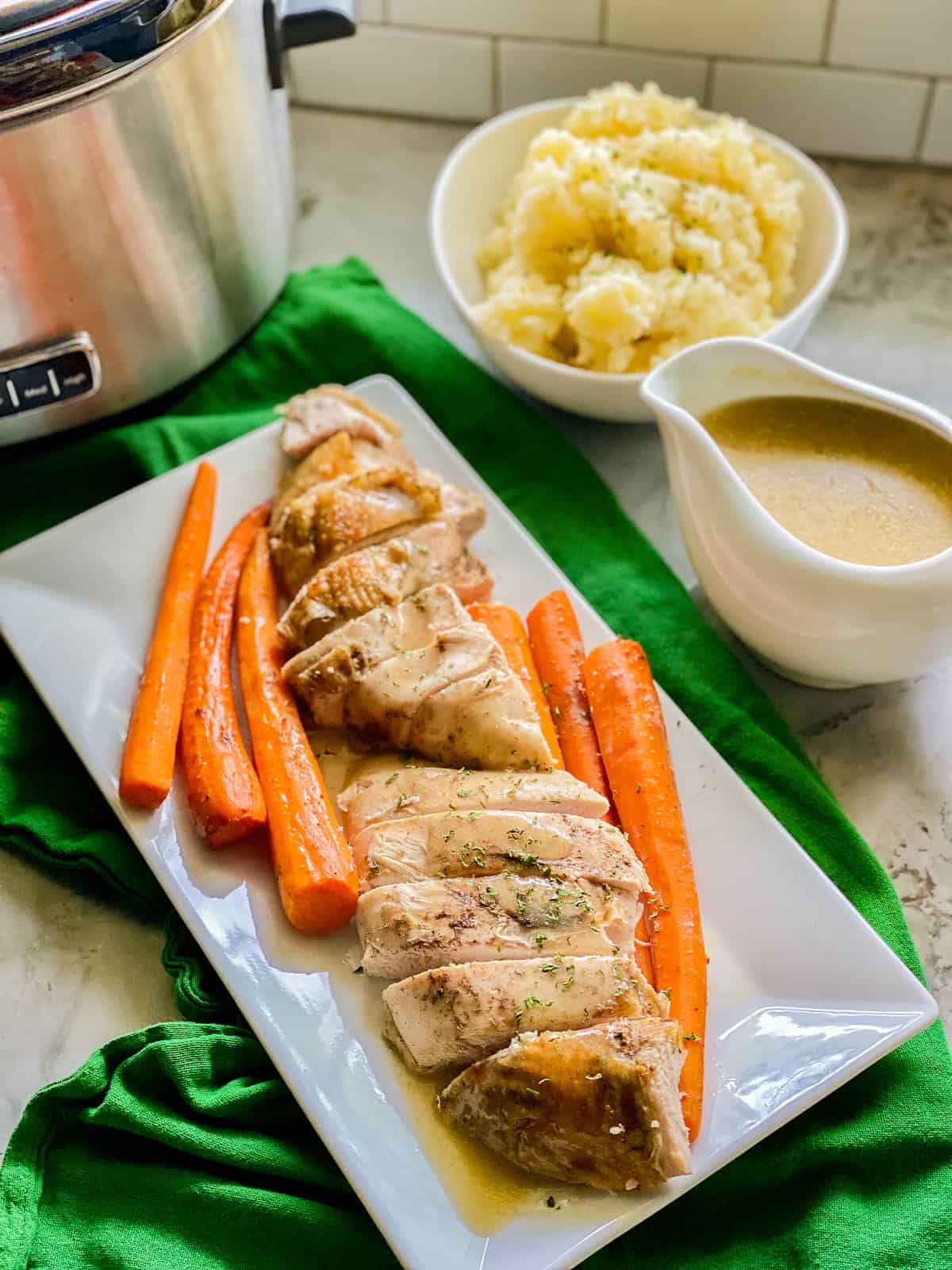 Sliced turkey breast and carrots with gravy and parsley on top of a white rectangular dish.