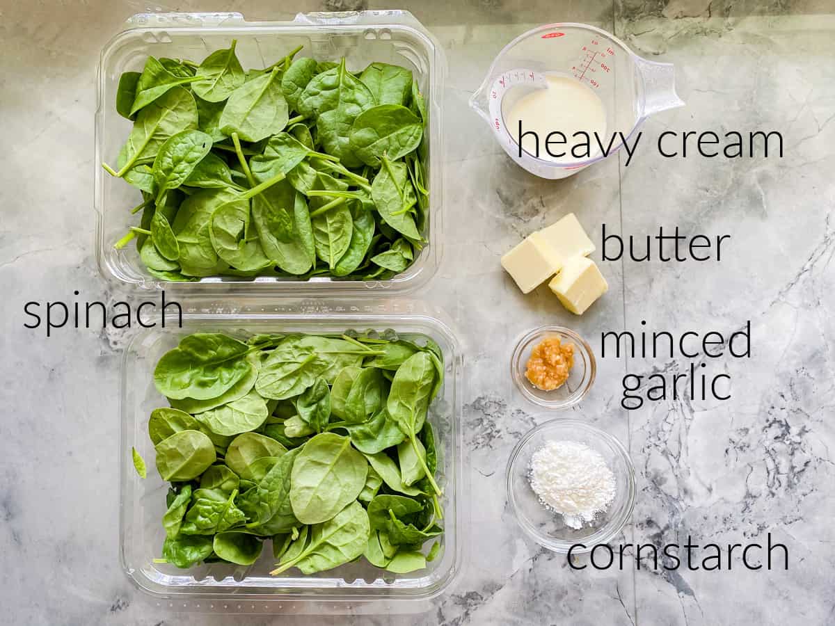 Ingredients on marble countertops; fresh spinach, heavy cream, butter, garlic, and cornstarch.