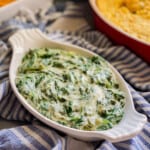 White oval dish filled with creamed spinach on a blue and white striped towel.