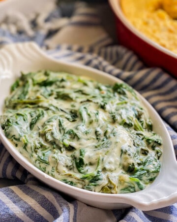 White oval dish filled with creamed spinach on a blue and white striped towel.