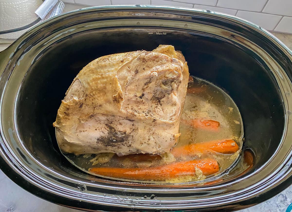 Black oval slow cooker with a cooked turkey breast and carrots.