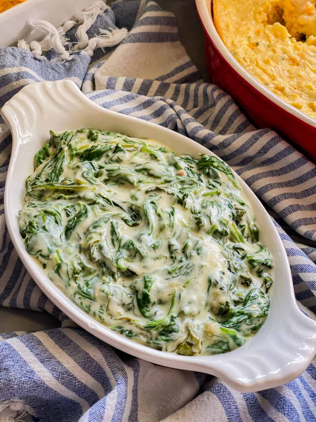 Oval baking dish with creamed spinach on a blue and white striped cloth.