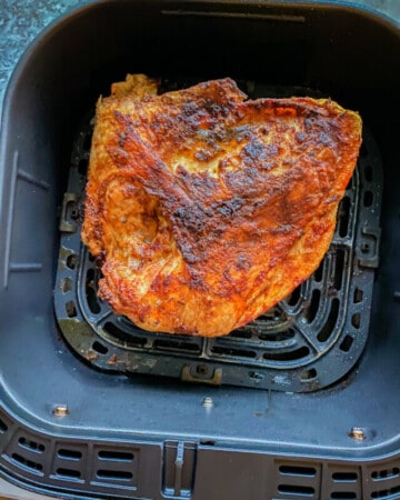 Black air fryer basket filled with a cooked half turkey breast.