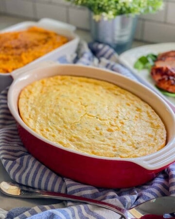 Red baking dish filled with corn casserole on a blue and white striped towel.