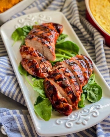 White platter sitting on top of a white and blue stripped cloth with turkey sliced on top of spinach.