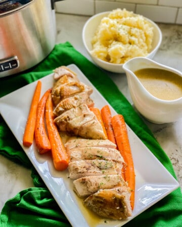 Sliced turkey breast and carrots with gravy and parsley on top of a white rectangular dish.