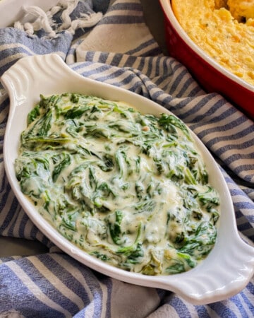 Oval baking dish with creamed spinach on a blue and white striped cloth.
