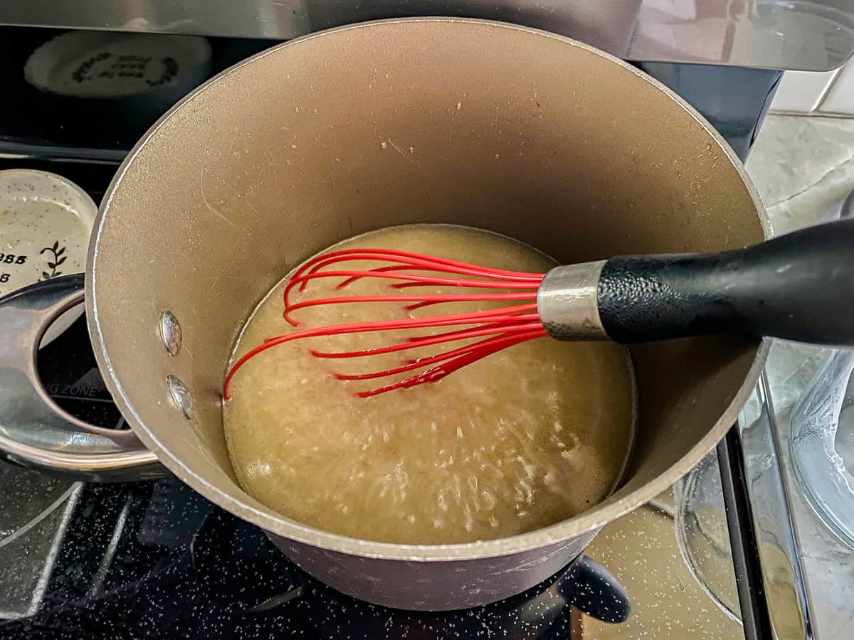 Brown sauce pan on a black stove top with a red whisk stirring gravy.