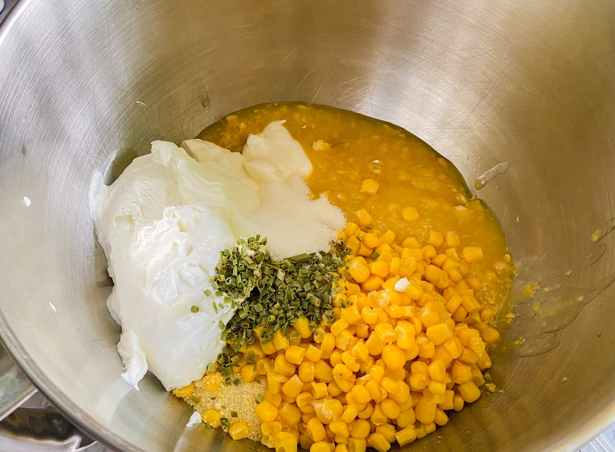 Silver mixing bowl with creamed corn, corn kernels, soure cream, sugar, and chives.