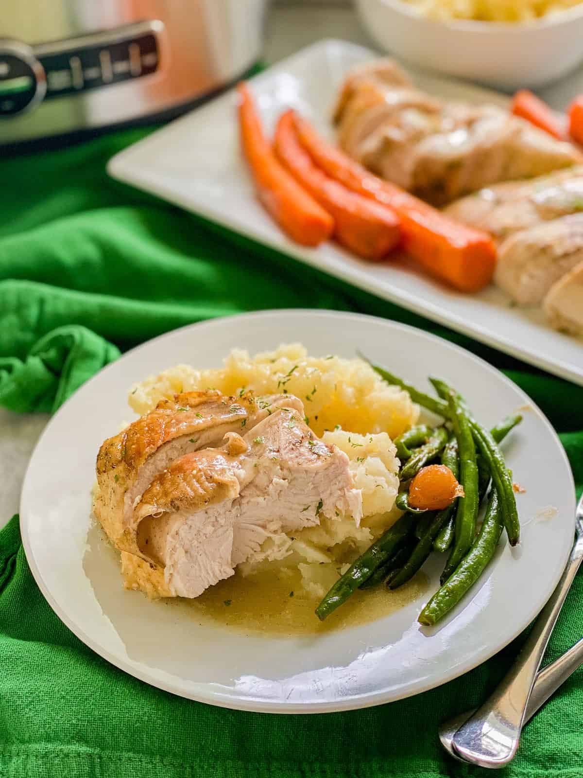 White dish on a green cloth filled with turkey, mashed potatoes, and green beans.