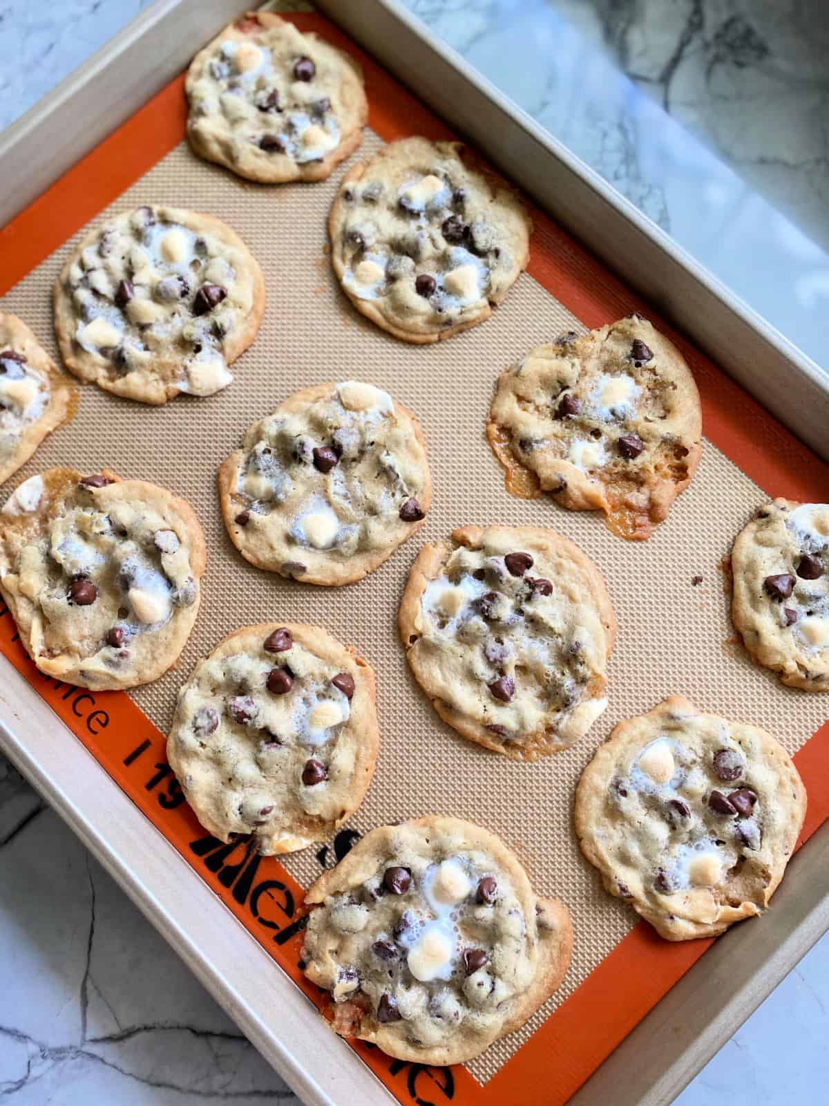 Baking sheet filled with 12 baked cookies on a marble countertop.