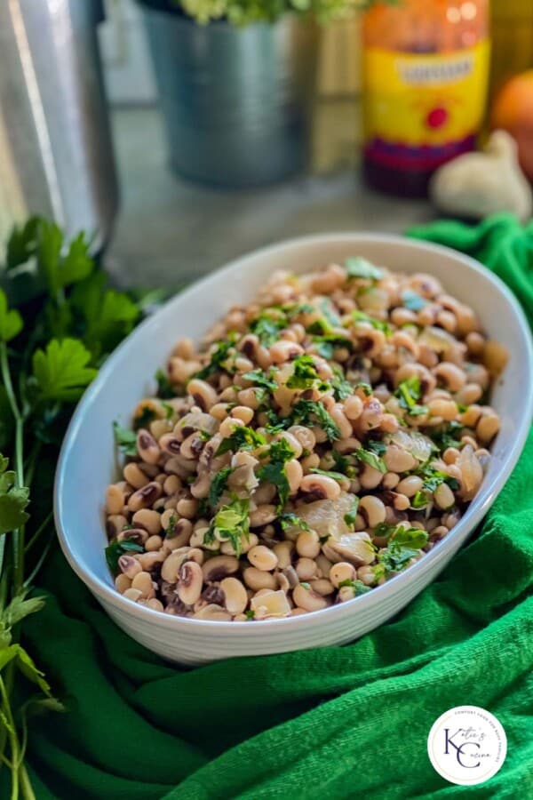 White oval dish filled with black eyed peas and fresh parsley with logo on bottom right corner.