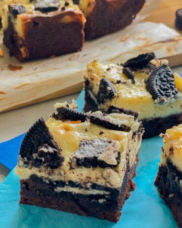 Three slices of brownie topped cheesecake bars with OREOs on a blue napkin.
