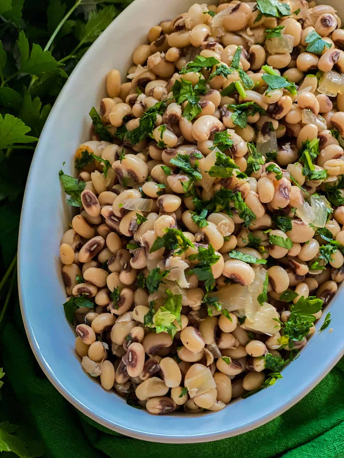 white oval bowl filled with black eyed peas with fresh herbs.