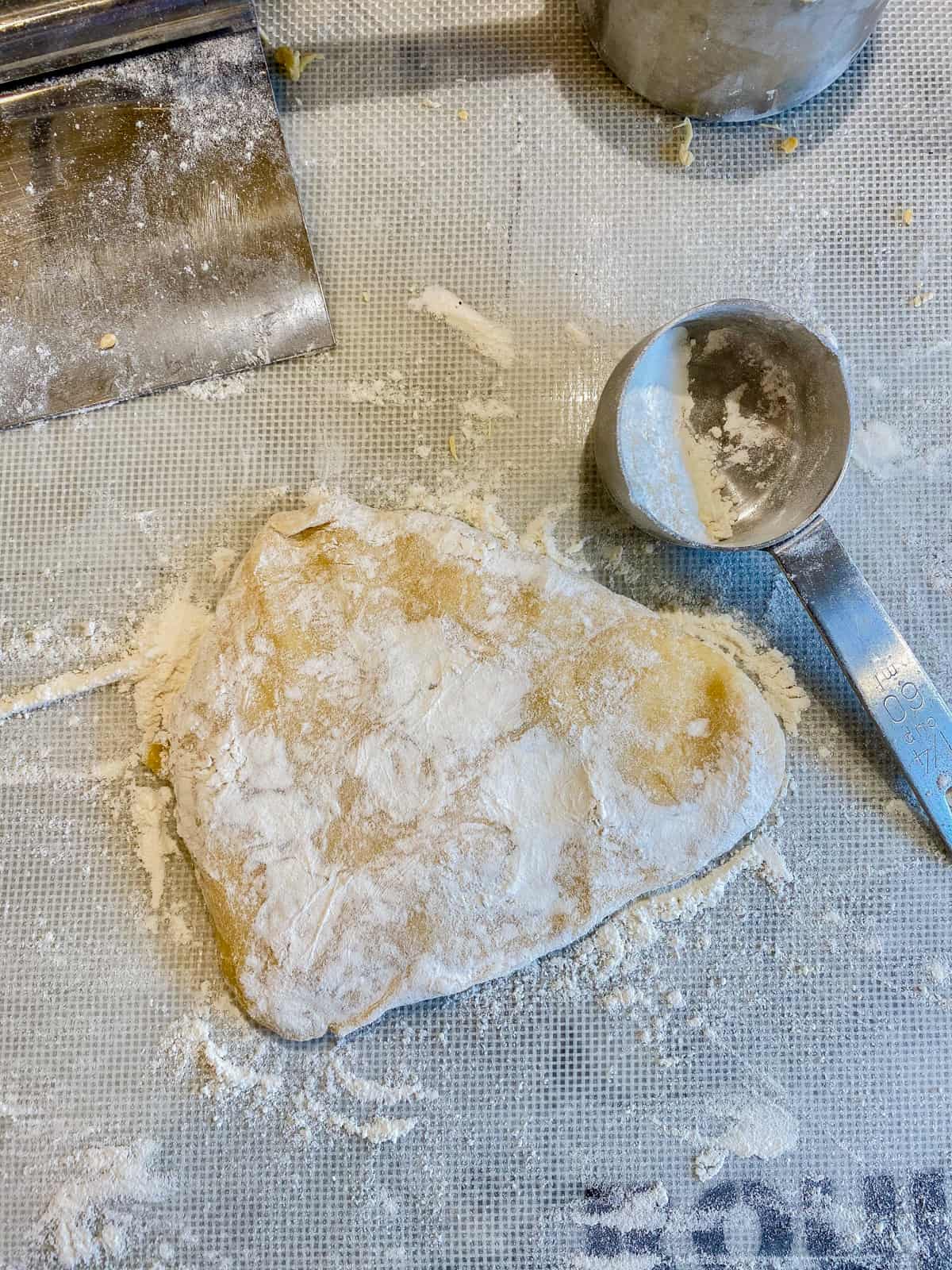 Dough with flour on top and a measuring cup next to it.