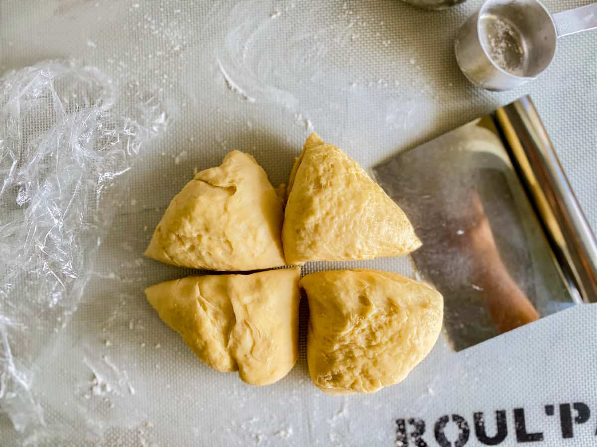 Round disc of pasta dough divided by four wedges with a bench knife next to it.