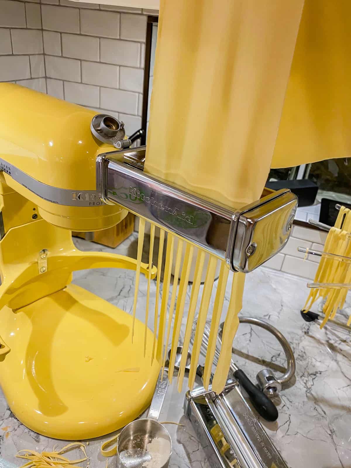 Pasta sheet being fed into a KitchenAid pasta attachment making pasta.